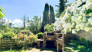 Ein rustikaler Garten mit einer Ziegelstruktur, üppigem Grün und weißen Blüten.