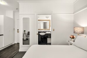 Une chambre à coucher moderne avec un grand lit, une coiffeuse blanche avec un miroir, une lampe de chevet et une vue sur la salle de bain.