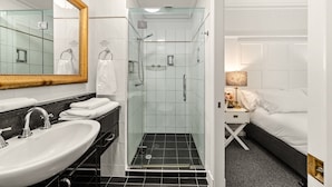 Un baño moderno con ducha acristalada, un lavamanos con encimera de mármol y una cama con ropa de cama blanca.