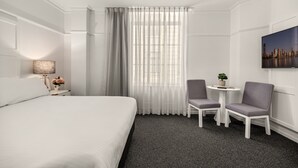 Habitación de hotel con una cama grande, una mesita con dos sillas, una lámpara y un cuadro en la pared.