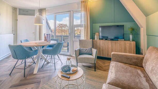 En moderne stue med et træspisebord, blå stole, en beige sofa og et fjernsyn på et træskab.