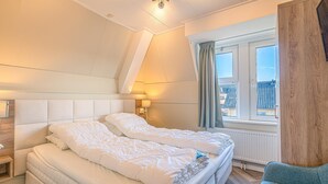 Et soveværelse med seng, natbord, lampe, vindue og udsigt over byen.