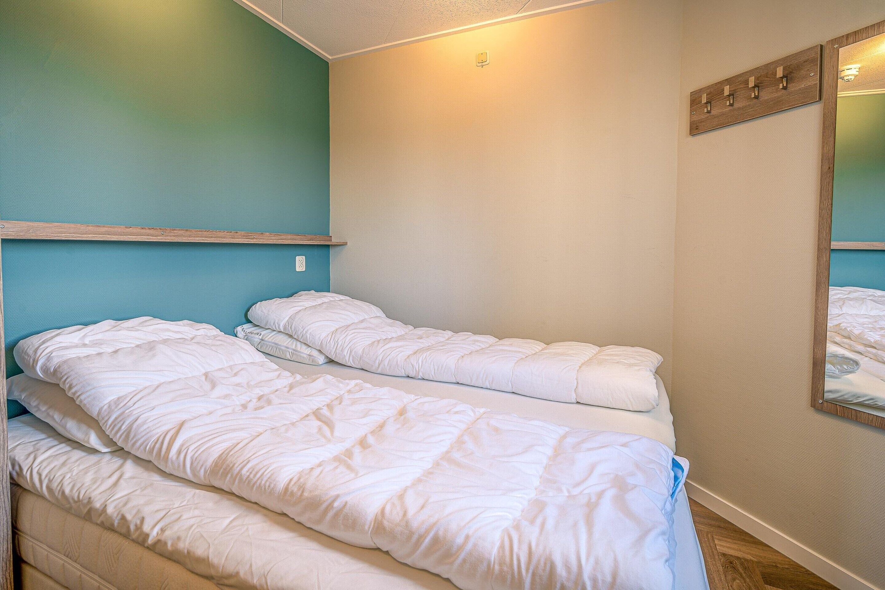 A bedroom with two single beds, a wooden shelf, a mirror, and a light fixture on the wall.