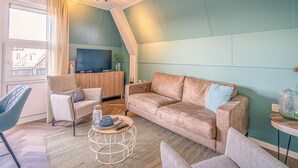 En stue med en beige sofa, en blå lænestol, et træ TV-bord og et lille sofabord.