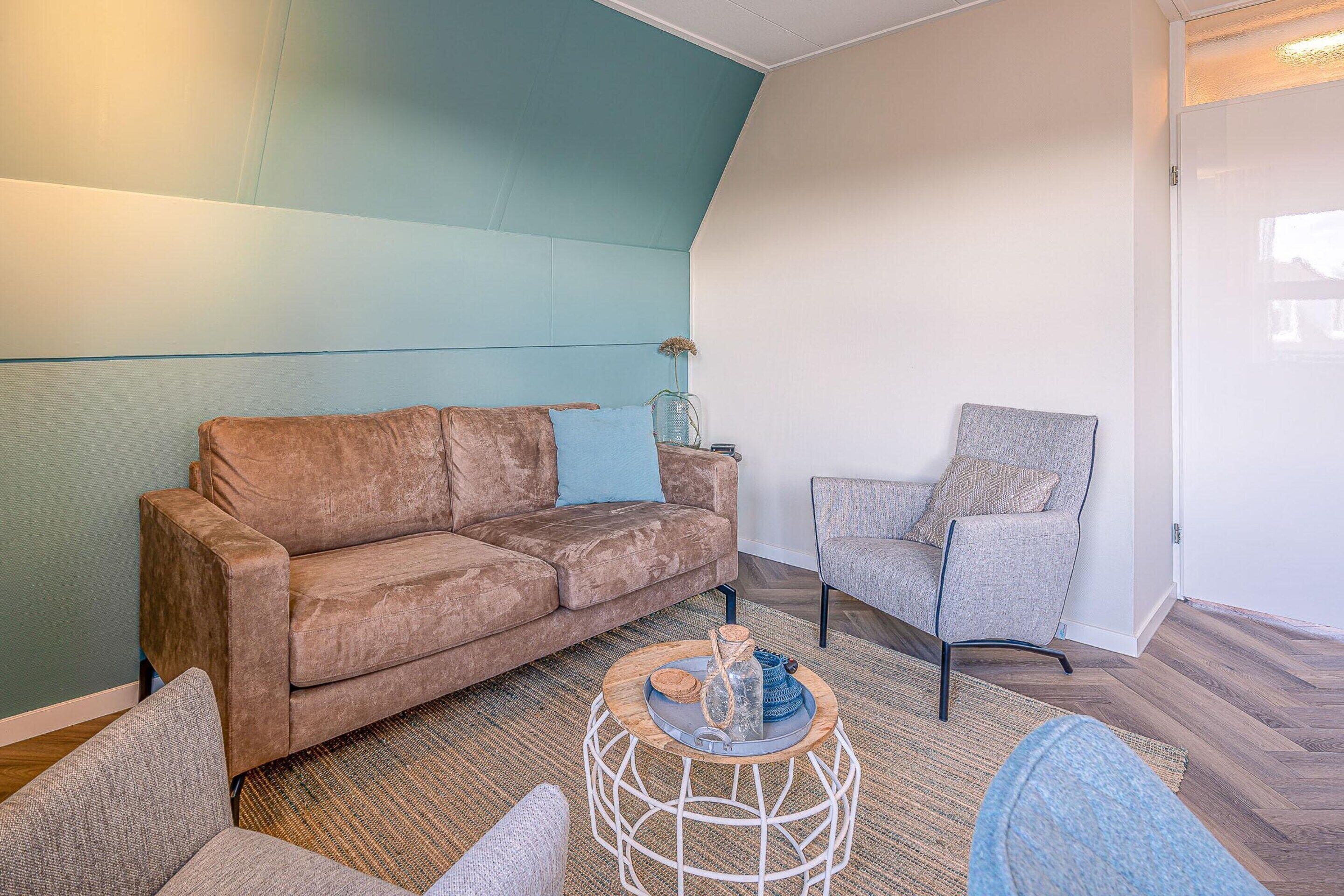 A living room with a brown sofa, a grey armchair, and a round coffee table with decorative items.