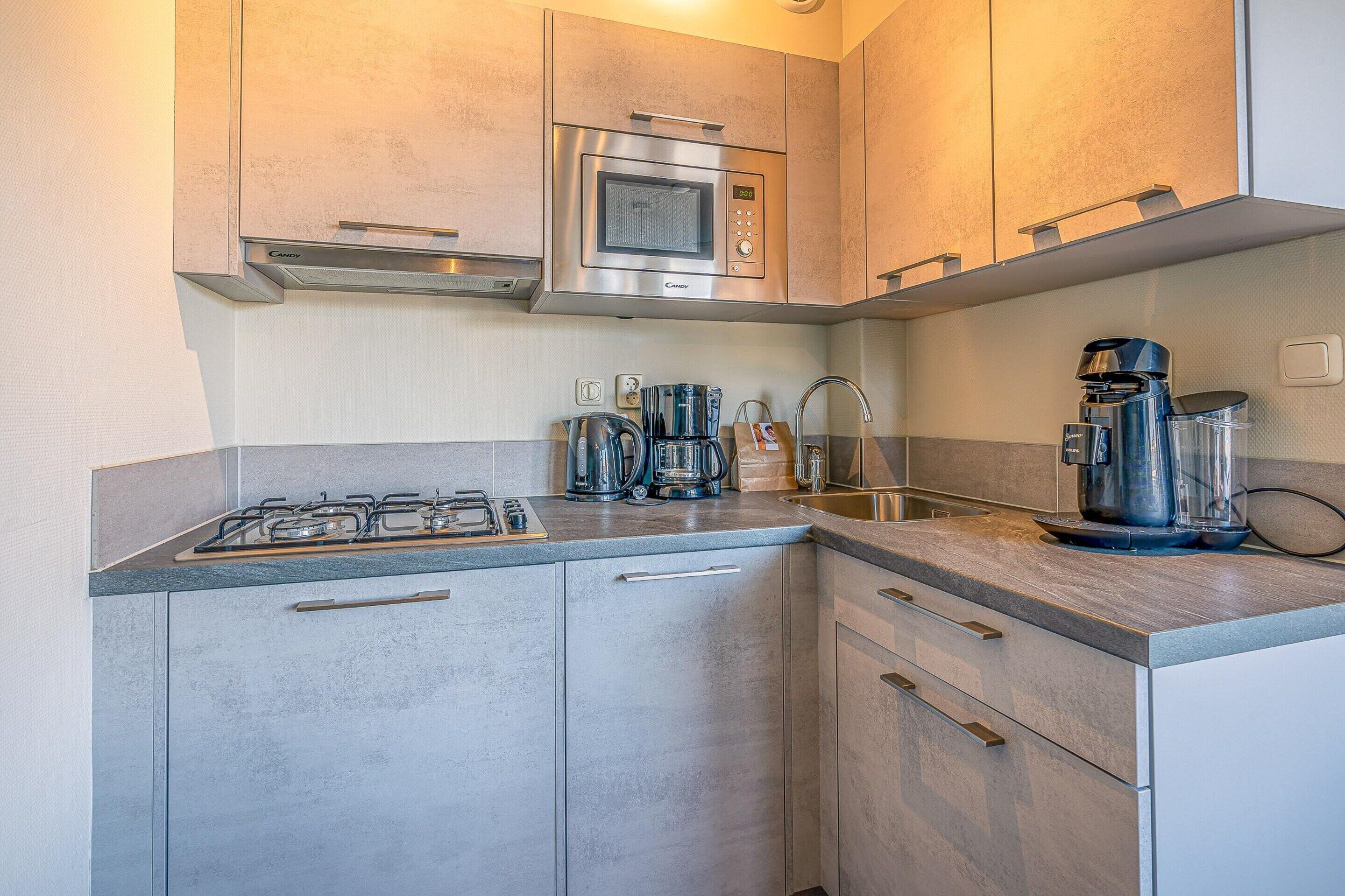 Una cocina compacta con estufa a gas, cafetera, microondas y pileta.