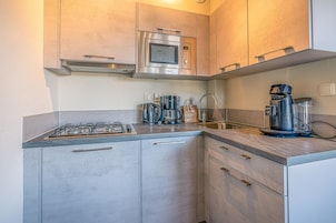 A compact kitchen with a gas stove, a coffee maker, a microwave, and a sink.