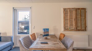 A dining area with a wooden table, cushioned chairs, a remote control, and a framed picture on the wall. - Charming Holiday Home for 2 People (De Koog)