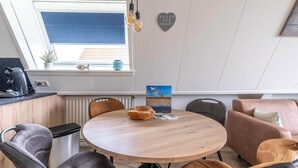 Un espace repas moderne avec une table ronde en bois, des chaises en cuir, une petite poubelle et une vue sur l’extérieur par une fenêtre.