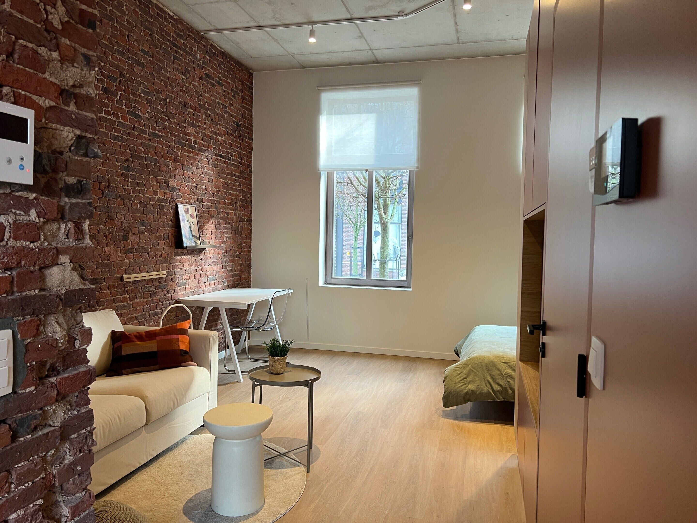 A modern living room with a brick wall, a white sofa, a small round table, and a window with a view of trees.