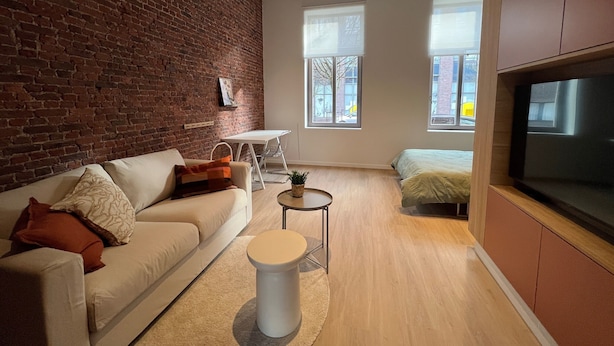 A modern living room with a brick wall, a sofa, a small table, and a TV. - Charming Ground-floor Apartment in Bree (Bree)