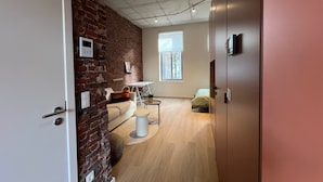 A modern interior with exposed brick walls, a wooden floor, a white door, and a window providing natural light. - Charming Ground-floor Apartment in Bree (Bree)