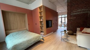 A modern bedroom with a bed, wardrobe, TV, and a dining area with a brick wall. - Charming Ground-floor Apartment in Bree (Bree)