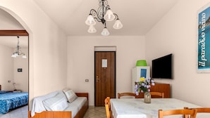Ein Zimmer mit Bett, einer Schlafcouch, einem Esstisch mit Stühlen, einem Fernseher und einer Wandleuchte.