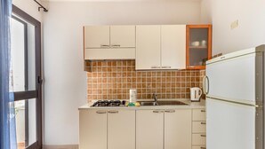 A compact kitchen with a gas stove, sink, and a white refrigerator. - 150 Meters From the Sea, 2 Swimming Pools (Valledoria)
