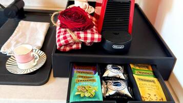 A tray with a coffee maker, a red rose, a cup of coffee, a napkin, and Twinings tea packets.