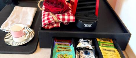 A tray with a coffee maker, a red rose, a cup of coffee, a napkin, and Twinings tea packets.