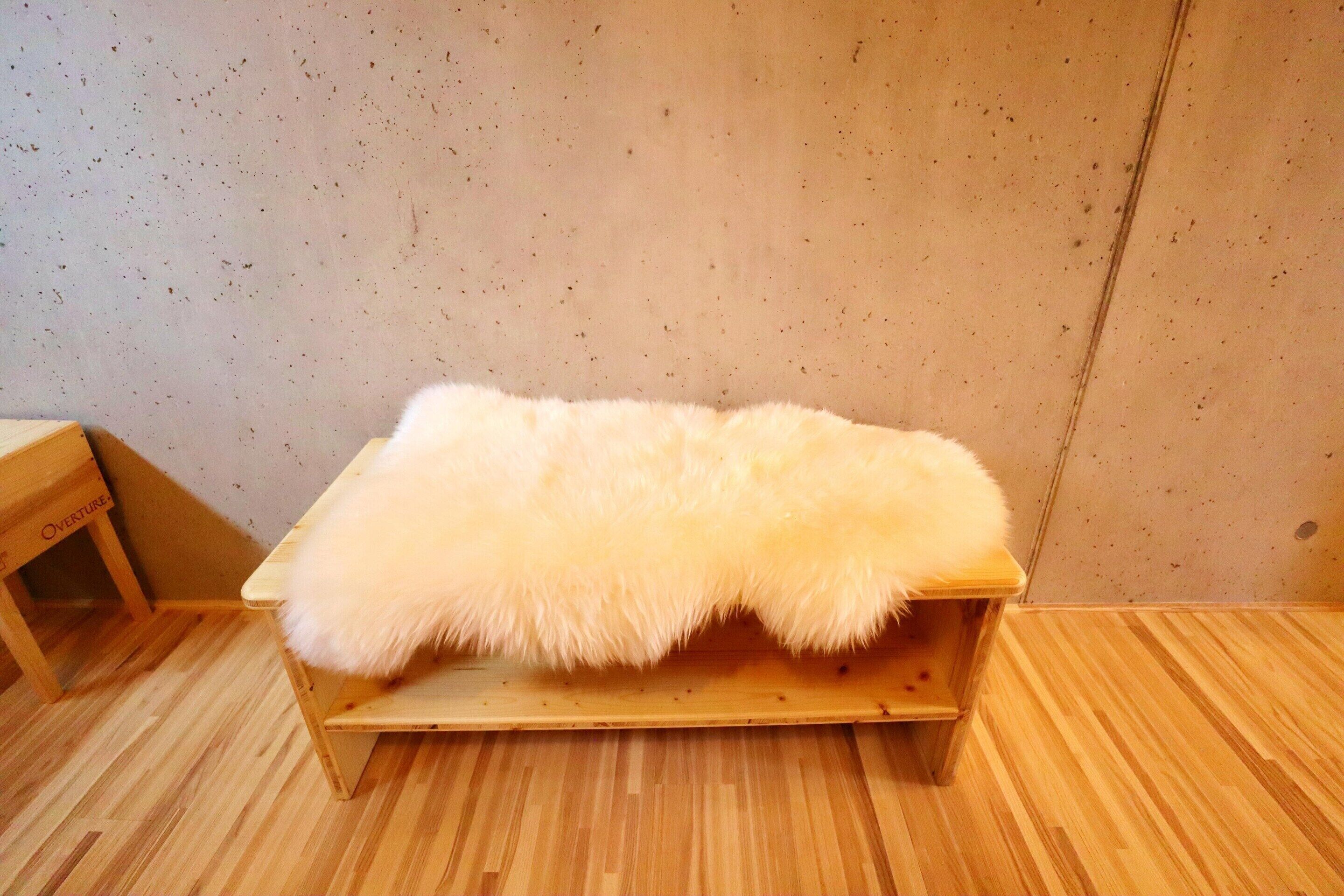 A wooden bench with a fluffy white cushion.