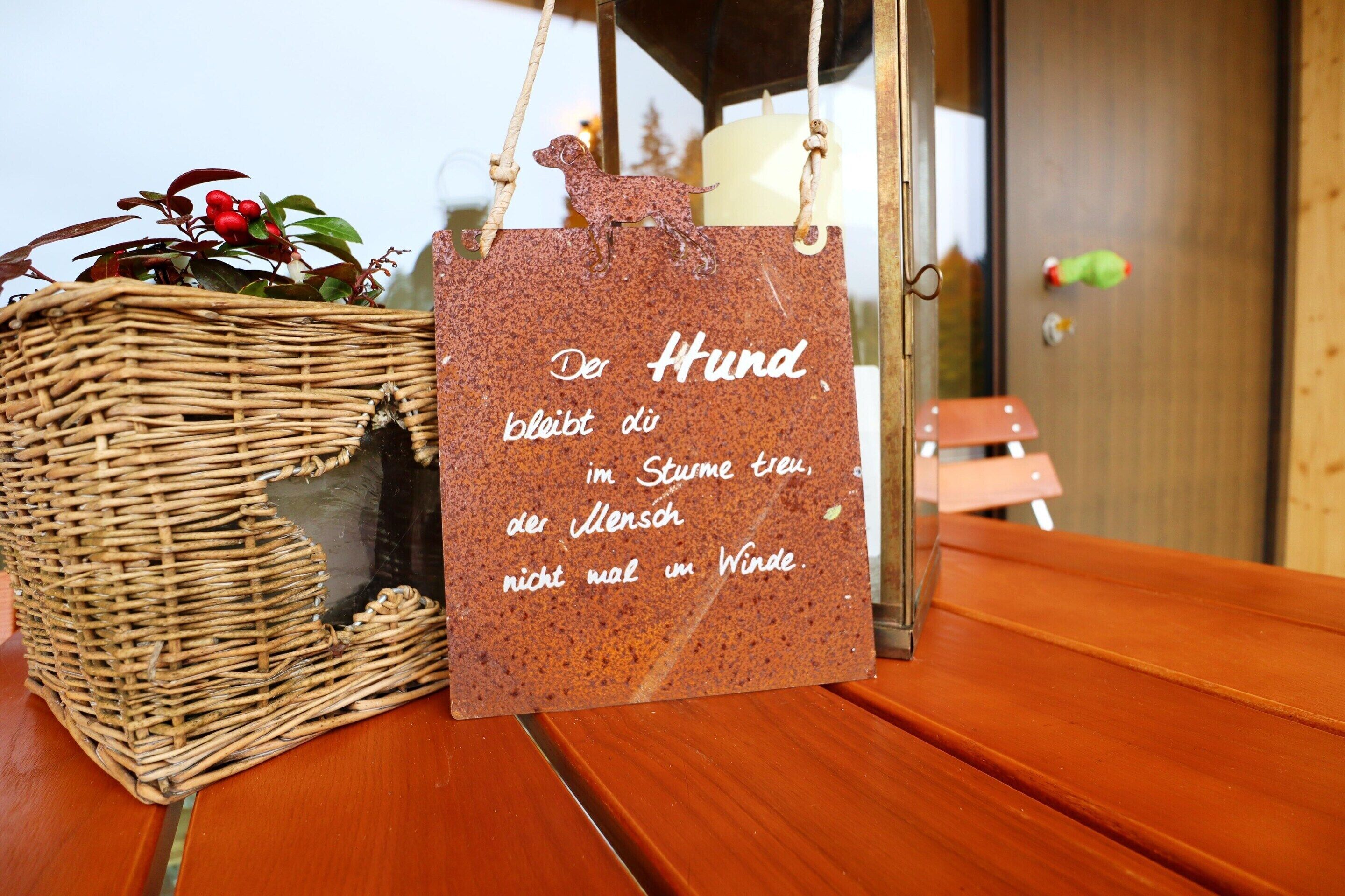 A wicker basket with a sign in German, a candle, and a toy dog on a wooden table.