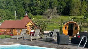 A swimming pool with lounge chairs, a wooden deck, and a wooden cabin in the background. - Finnish Kota with Jacuzzi, sauna, heated swimming pool and wellness treatments (Voissant)