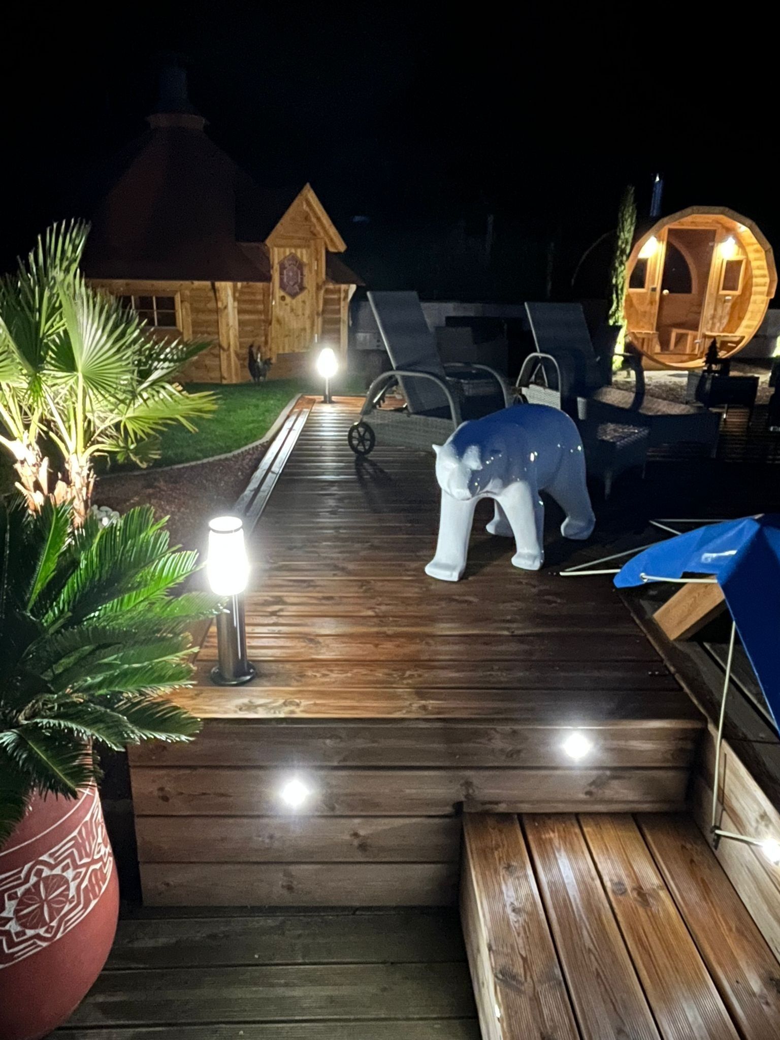 Une terrasse en bois avec un banc, une petite maison et une structure circulaire en bois illuminée.