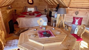 A cozy wooden cabin with a loft bedroom, a dining area with a round table, and a small kitchen area. - Finnish Kota with Jacuzzi, sauna, heated swimming pool and wellness treatments (Voissant)
