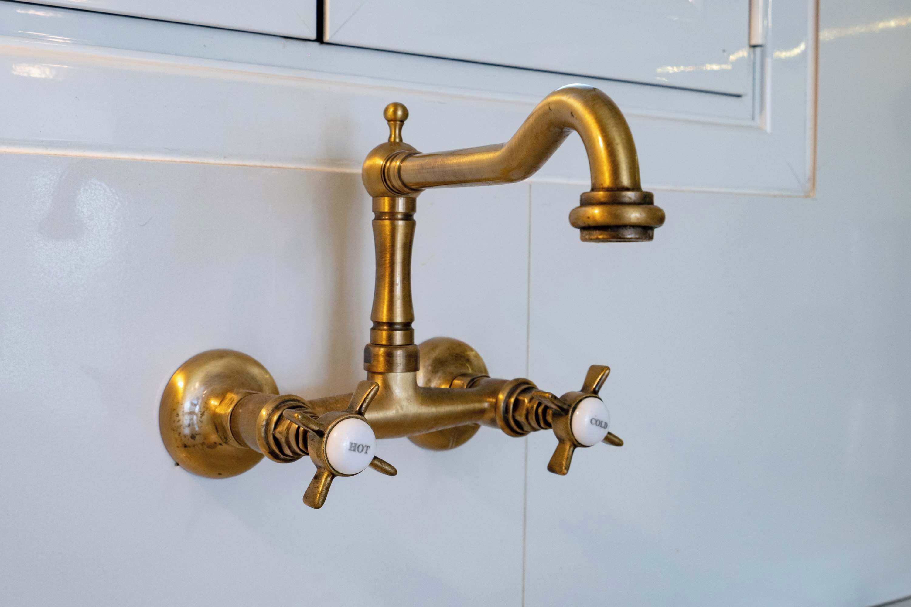 Un robinet en laiton avec des poignées pour l’eau chaude et l’eau froide, fixé sur un mur blanc.