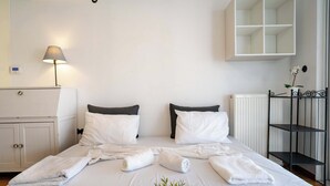 A neatly made bed with white linens and towels, a bedside lamp, a white wardrobe, and a radiator. - City Panorama Studio by ΜΡS (Athens)