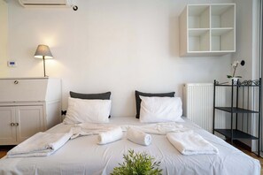A neatly made bed with white linens and towels, a bedside lamp, a white wardrobe, and a radiator. - City Panorama Studio by ΜΡS (Athens)