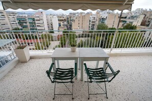 Un balcón con una mesa, sillas, una planta en maceta y vistas de la ciudad.