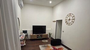 A living room with a sofa, a TV, a clock, and a plant. - IRIDE HOME _ Wellness & Relaxation (Bergamo)