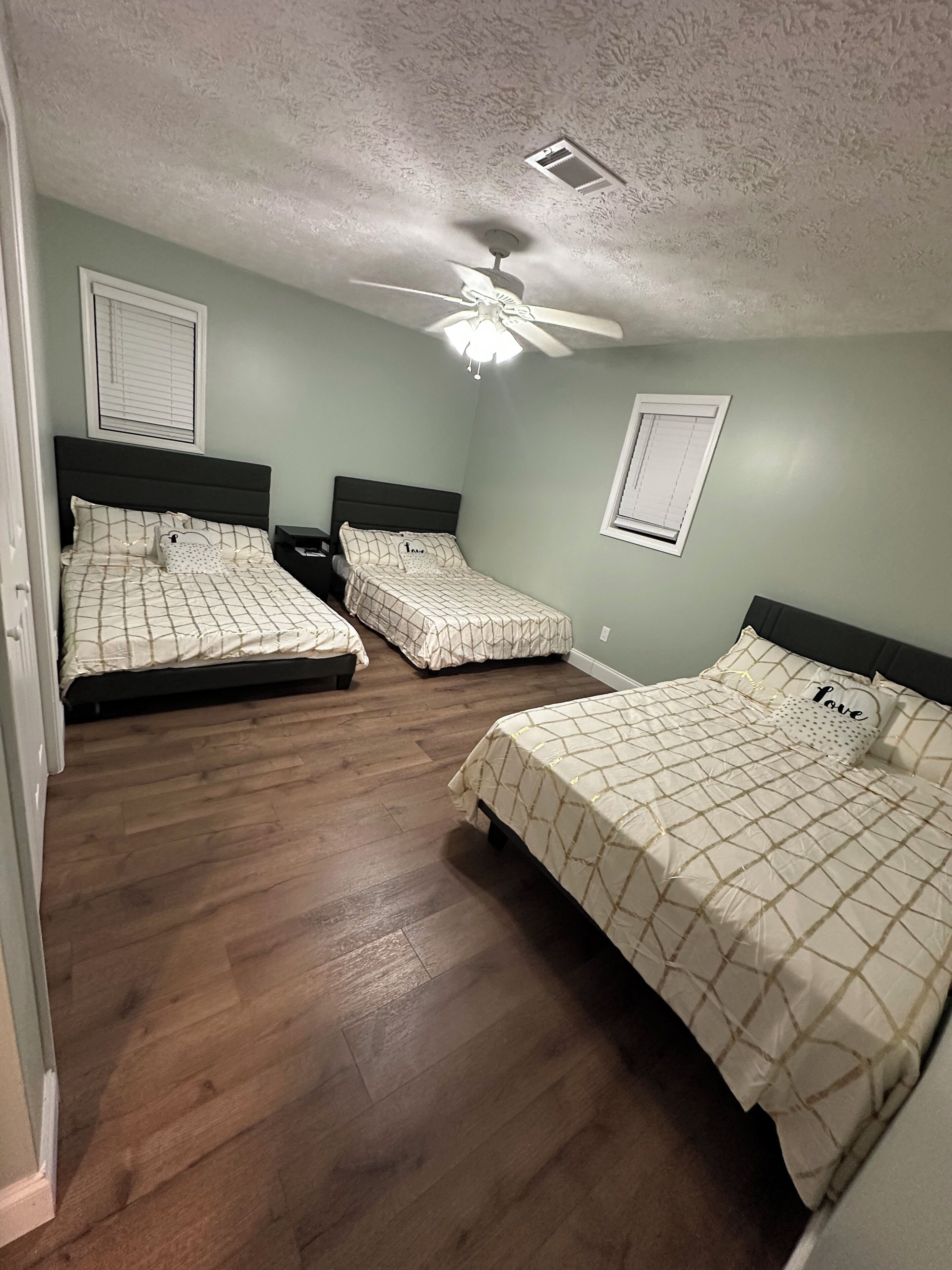 A bedroom with three beds, a ceiling fan, and a window with blinds.