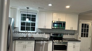 A modern kitchen with white cabinets, stainless steel appliances, a hexagonal tile backsplash, and a window with blinds. - Luxurious 5-bedroom house with Game Room in Stone Mountain (Stone Mountain)