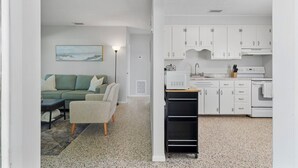 A modern kitchen with white cabinets, a microwave, and a stove. There is a dining table with chairs and a sofa in the adjacent living area. - Cozy Cottage Minutes from the Beach (Sarasota)