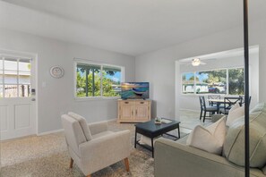 Ein Wohnzimmer mit Fernseher, einer Couch, einem Couchtisch und einem Essbereich mit Tisch und Stühlen.