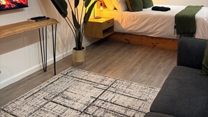 Tunnelmallinen makuuhuone, jossa on sänky, yöpöytä ja televisio, josta näkyy takkatuli.