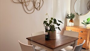 Ruokailutila, jossa on puinen pöytä, valkoiset tuolit, puinen lipasto ja koristeellinen seinätaideteos.