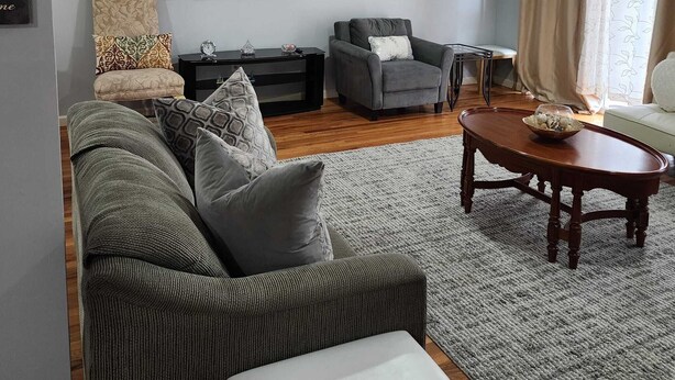 Ein Wohnzimmer mit grauem Sofa, grauem Sessel, Couchtisch aus Holz und einem flachbildfernseher an der Wand.