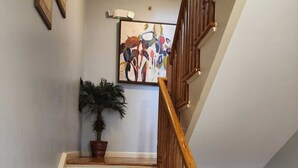 Eine Treppe mit Holzboden und einem Holzgeländer, die zu einer Zwischenebene mit einem Blumentopf und einem farbenfrohen, abstrakten Gemälde führt.