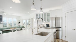 A modern kitchen with white cabinetry, stainless steel appliances, and a large island with a sink. - Steps to the Beach: 6BR Gem / Ocean Views / BHI + Shoals Club / 2 Carts (Bald Head Island)