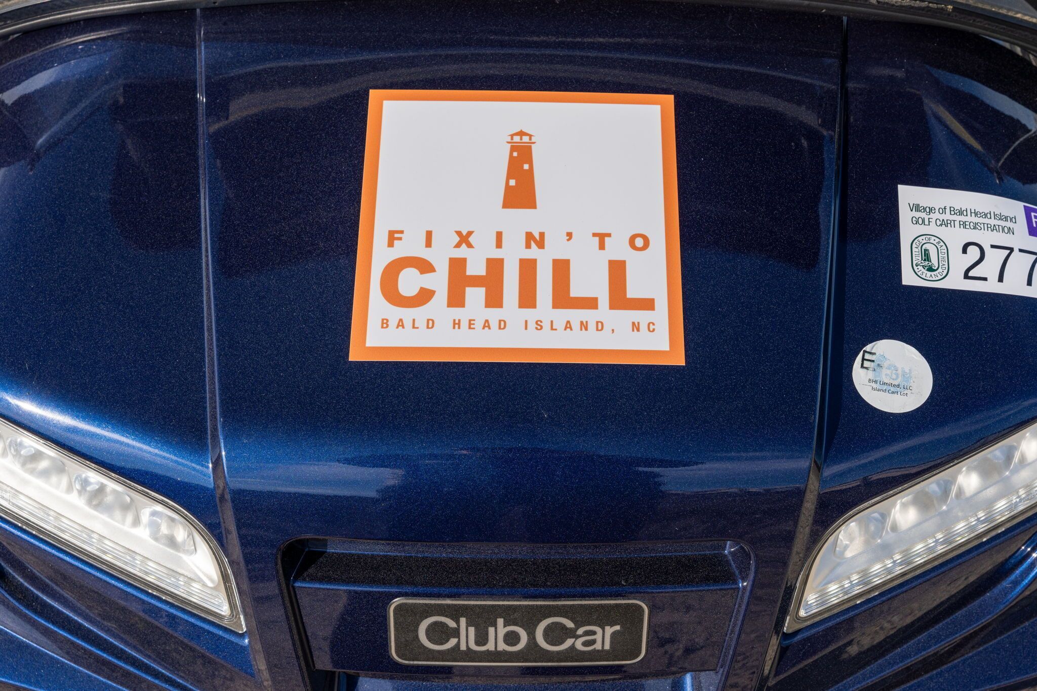 Un vehículo Club Car con un adhesivo que dice 'Fixin' to Chill', una etiqueta que indica 'Bald Head Island, NC' y un adhesivo de registro '277'.