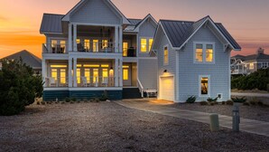 A two-story house with a balcony, a garage, and a driveway. - Steps to the Beach: 6BR Gem / Ocean Views / BHI + Shoals Club / 2 Carts (Bald Head Island)