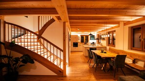 A wooden staircase leading to a dining area with a kitchen in the background. - Heimatzeit - Chalet with whirlpool and sauna (Reichenbach)