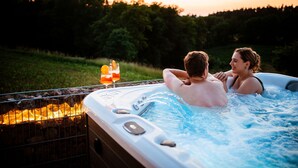 A hot tub with a glass of orange juice and a candle, surrounded by a metal fence and a grassy area. - Heimatzeit - Chalet with whirlpool and sauna (Reichenbach)