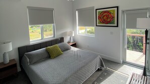 Une chambre moderne avec un grand lit, deux tables de chevet, un luminaire au plafond et une fenêtre donnant sur un paysage verdoyant.