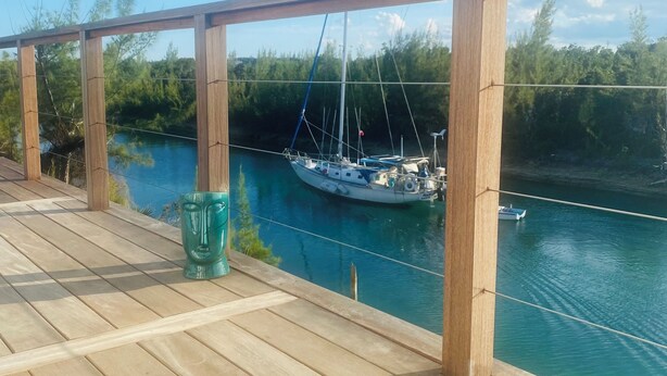Une terrasse en bois donnant sur une rivière, avec un voilier amarré.