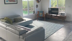 Un vaste salon doté d’un canapé d’angle gris, d’un téléviseur à écran plat posé sur un meuble en bois et d’un ventilateur de plafond.