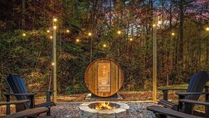 Un espacio al aire libre acogedor con sillas Adirondack, un hogar de piedra y un barril de madera.