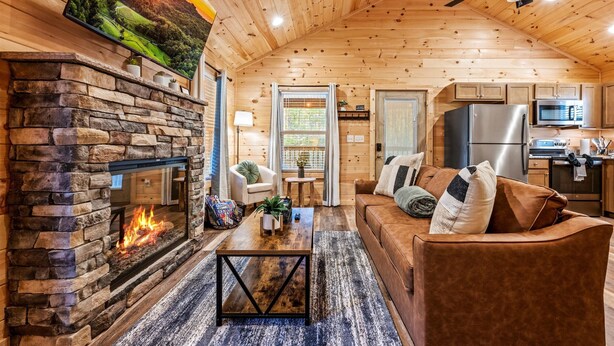 Un acogedor interior de cabaña con chimenea de piedra, techo de madera y sala de estar con sofá y mesa de centro.