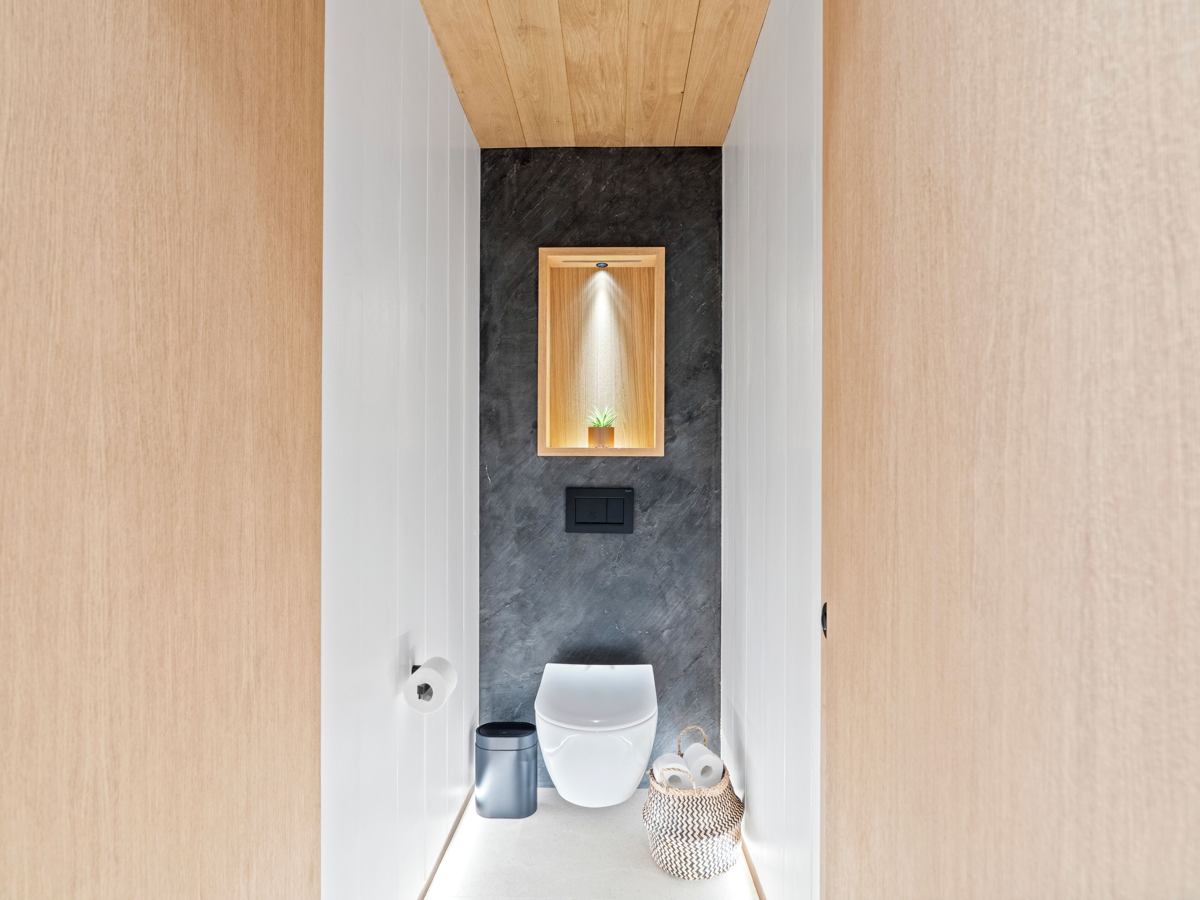 Un baño moderno con un inodoro blanco, un cesto de basura pequeño y una cesta decorativa.